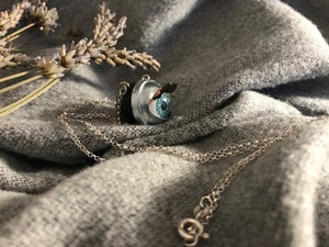 Side view of aqua doll eye necklace displaying the lashes that will flutter when the doll eye blinks
