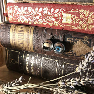 close up of blinking eye earrings hung on vintage books, eyes are blue