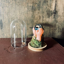 Load image into Gallery viewer, image with dark wood background showing the small glass dome removed from the base, showing the doll hands, eye and moss inside. 