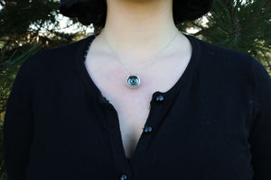 Modeal wears black cardigan showing eyeball necklace resting on chest 