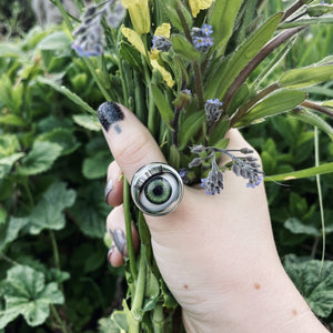 Green doll eye ring shown being worn on a thumb, whilst holding a bunch of wildflowers