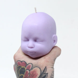 Purple doll head candle being balanced on tattooed hand
