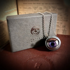 Purple doll eye necklace shown with grey packaging and silver foil design