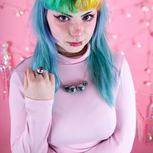 Large spider necklace with 4 doll eyes, and purple ring being worn by cute  model with pastel goth style and rainbow hair