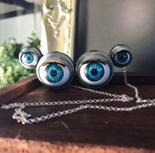 Load image into Gallery viewer, Large necklace made from 4 blinking doll eyes attatched together to form the shape of spider eyes, displayed on wooden background