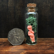 Load image into Gallery viewer, minature doll encased in glass vial with moss, shown with a 50 pence coin for size reference, the coin is a little under hald the height of the bottle.