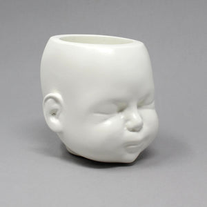 Doll head pot in matte white shown on grey background, the eyes are closed and looks like a sleeping doll