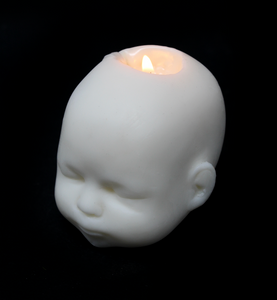 white doll head shaped candle shown burning with flame on black background