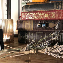 Load image into Gallery viewer, blinking doll eye earrings  shown hanging on vintage books