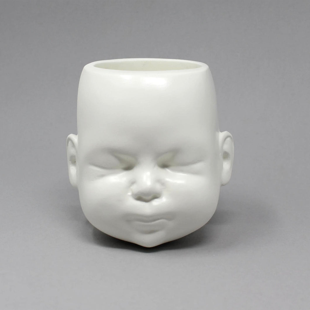White pot in the shape of a doll head on grey background