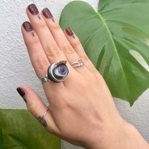 purple doll eye ring won on finger showing hand with leaves in background