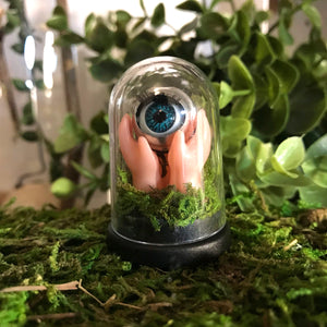 jawline jewellery minature curiosity diorama dome made from blinking doll eye and hands pushing up from the earth, made with real moss. This dome is plastic and comes with a black base 
