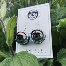 Load image into Gallery viewer, grey doll eyes in silver and black casing shown on packaging, a black and white backing card with jawline jewellery eye logo, displayed in plants