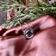 brown blinking doll eye necklace laying on it's side on dark pink silk