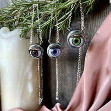 Load image into Gallery viewer, selection of three eyeball necklaces, brown purple and green hung on rosemary with dark wooden background