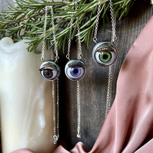 selection of three eyeball necklaces, brown purple and green hung on rosemary with dark wooden background