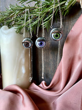 Load image into Gallery viewer, blinking eyeball necklaces hanging from rosemary branch with dark wood and candle behing
