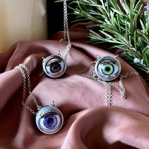 three jawline jewellery eyeball necklaces shown on dusky pink silk with candles and rosemary in the background