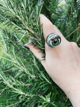 Load image into Gallery viewer, green doll eye ring shown on models hand holding a bunch of rosemary, the iris is a similar colour to the rosemary
